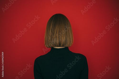 Print op canvas Woman in black sweater and with hairstyle bob isolated on red background, standing with her back to the camera
