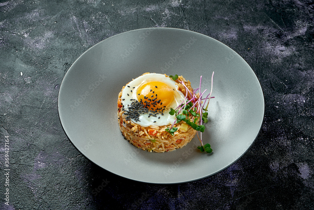 Rice fried in a wok with chicken and fried eggs in a gray plate on a black background. Asian street food