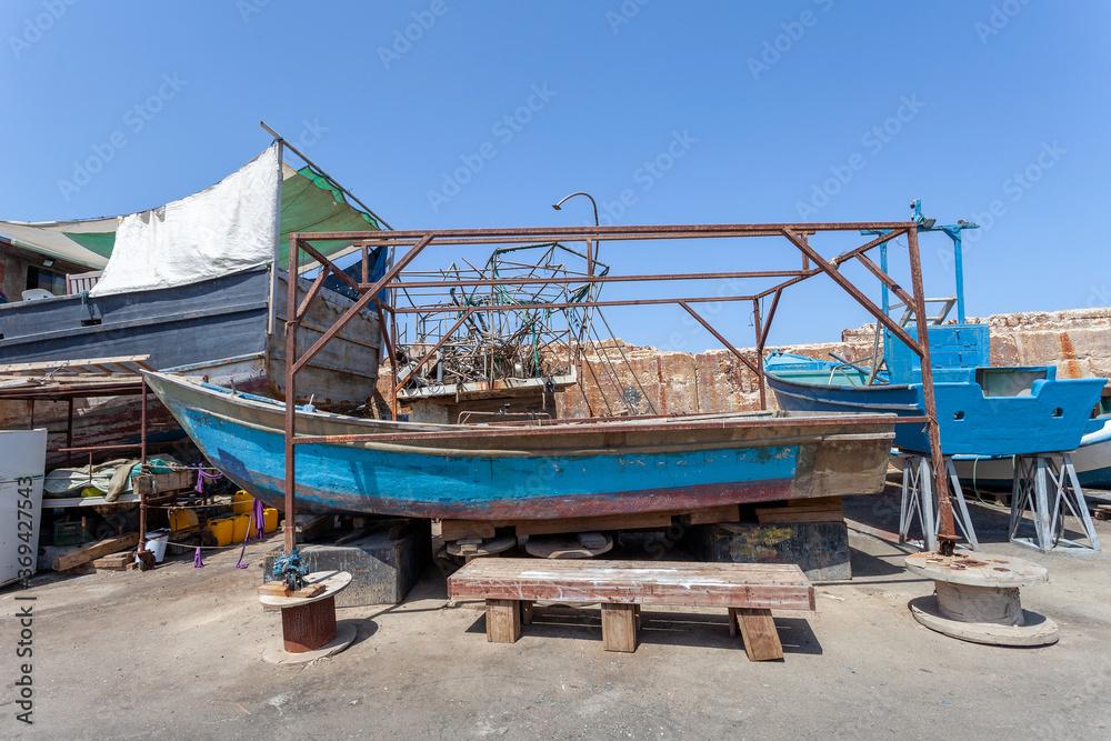 Old fishing boat in a dry dock, with blue sky in the background.
