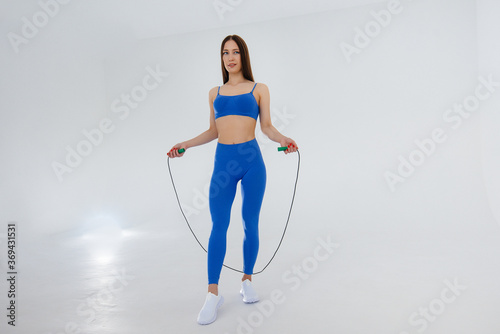 Sexy young girl jumping rope in a blue tracksuit on a white background. Fitness, healthy lifestyle © Andrii