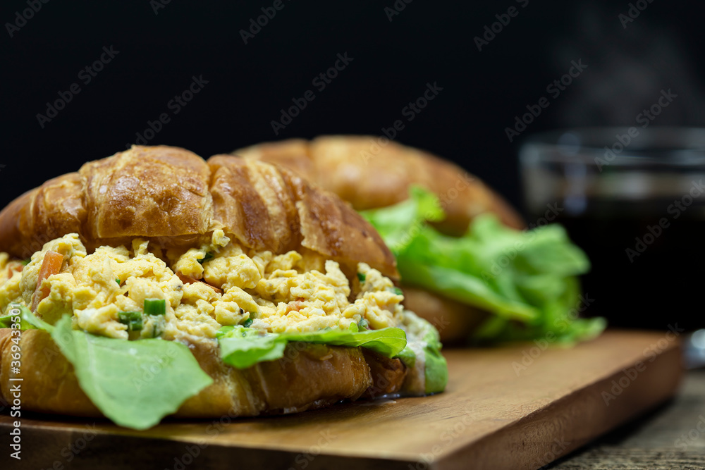 Close up Croissant stuffed scrambled eggs on wooden tray with hot coffee background. Close up Croissant stuffed scrambled eggs on wooden tray with hot coffee background.