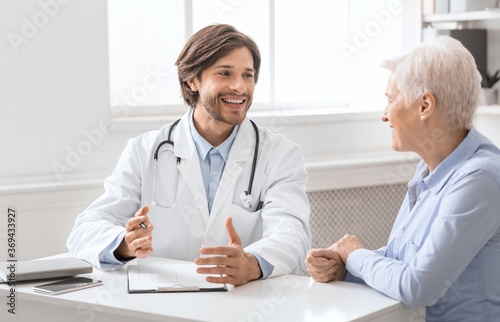 Friendly geriatrician talking with female patient, filling medical history photo