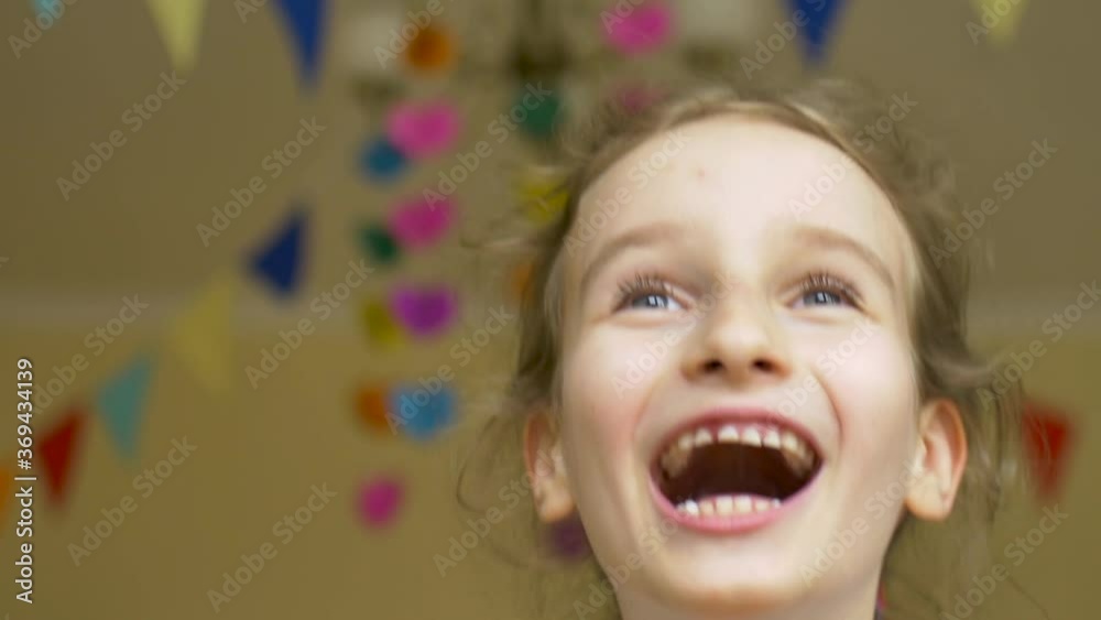 Kid's birthday party. Little laughing cute girl is celebrating her b-day with the colorful balloons on paper garland background at home Kid's birthday party. Little laughing cute girl is celebrating her b-day with the colorful balloons on paper garland background at home