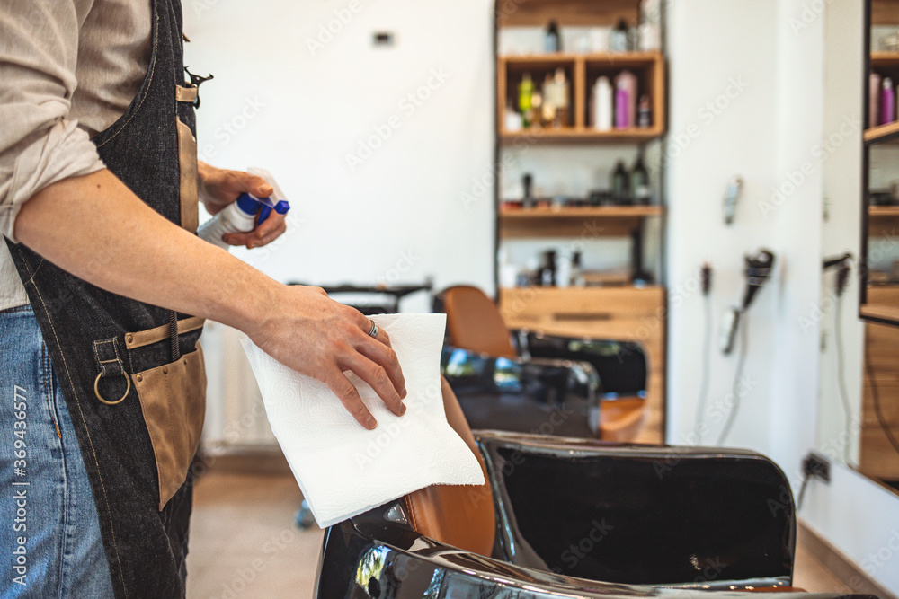 Male Barber cleaning equipment with alcohol spray before hair cut he wearing face mask prevention business reopening after coronavirus lockdown, Men's hairstyling new normal lifestyle.