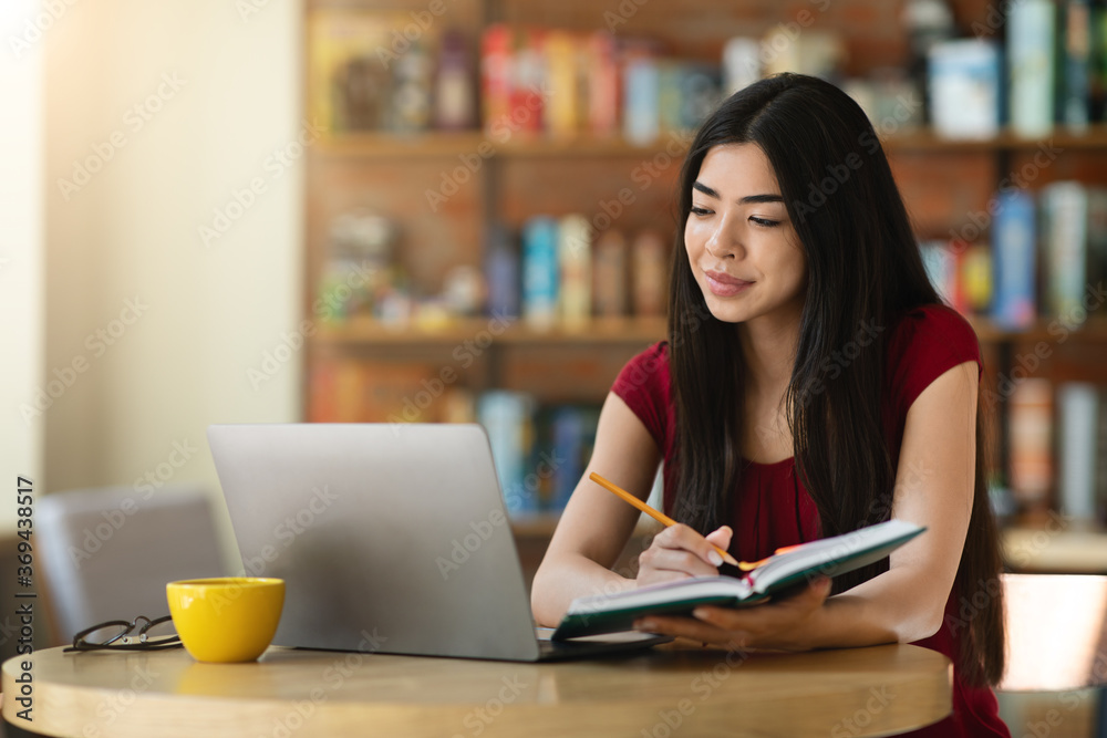 Online Education. Korean girl studying with laptop at cafe and taking notes Online Education. Korean girl studying with laptop at cafe and taking notes