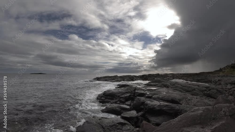 Small waves lapping against black rocks under cloudy dramatic sky in Norway. Rain in the distance. Small waves lapping against black rocks under cloudy dramatic sky in Norway. Rain in the distance.