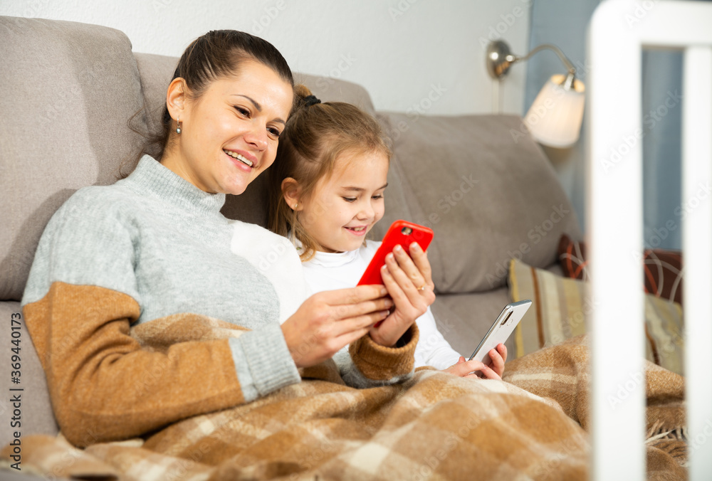 Mom and small daughter using smartphone in home interior