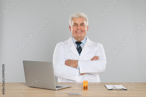 Professional pharmacist with laptop at table against light grey background
