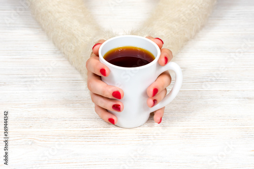 Female hands hold a white cup against the background of a white fluffy sweater with a beautiful red winter manicure. Drink, fashion, morning. New Year. Celebration. Tea coffee.