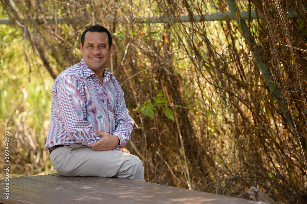 Portrait of happy overweight Indian businessman at the park outdoors Portrait of happy overweight Indian businessman at the park outdoors