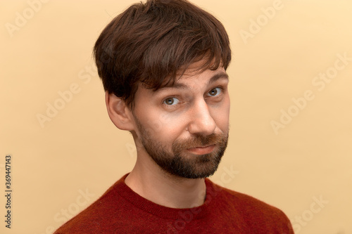 Is it. Photo of young man with beard wearing sweater, looking at camera with question, posing against yellow background photo
