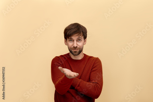 Just do this. Photo of young man with beard wearing sweater, holding hand with plam and asks something, has confident expression, posing against yellow background photo