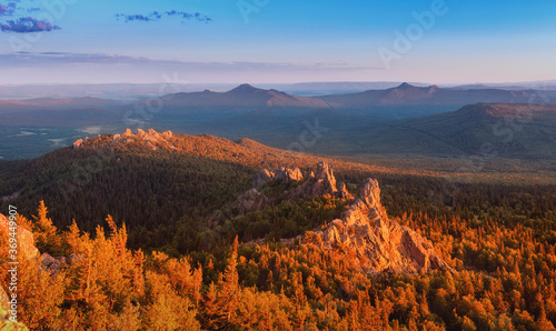 A rocky mountain range covered with forest is illuminated by the pink light of the setting sun. A natural Park or reserve or hunting grounds. Recreational tourism