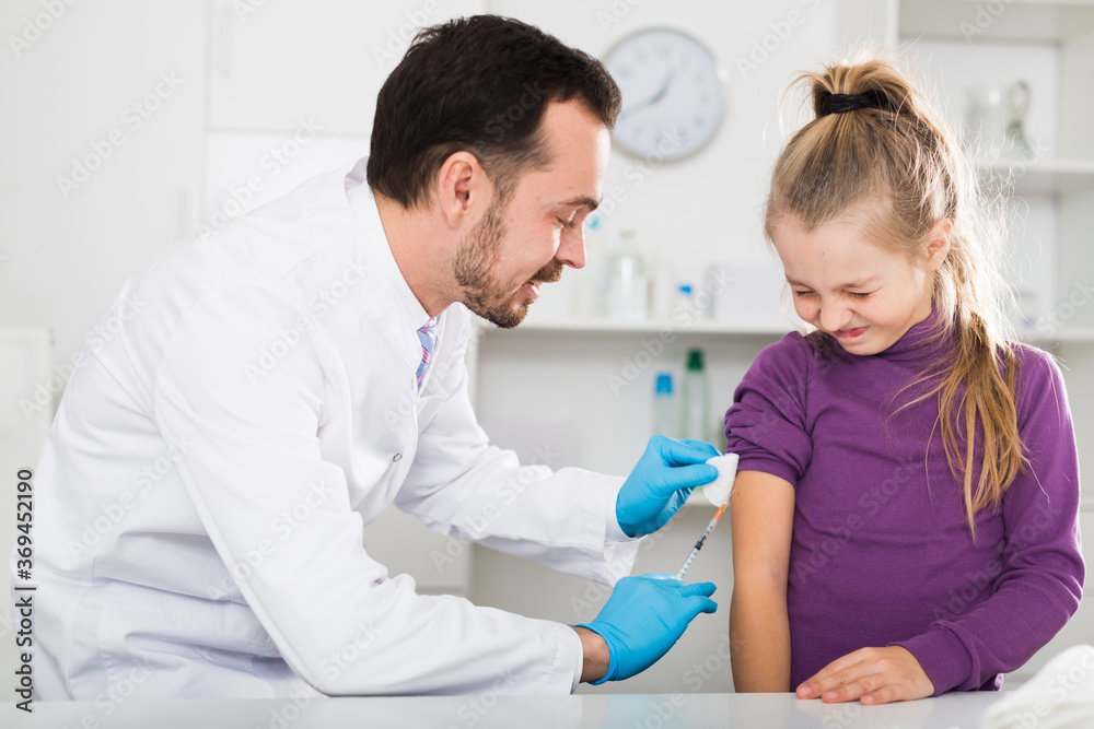 Fototapeta premium Male doctor using syringe to make injection to young female patient in hospital
