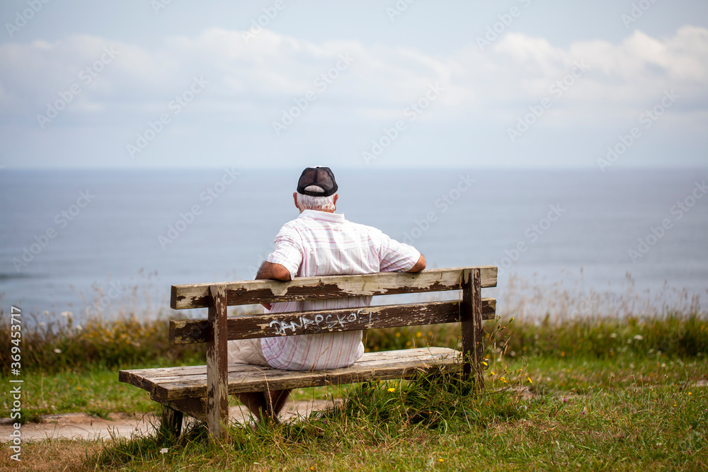 Hombre mayor sentado en banco de madera contemplando el mar Hombre mayor sentado en banco de madera contemplando el mar