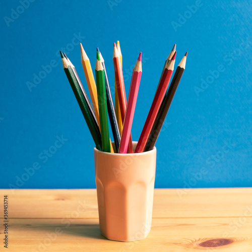 Color pencils in holder on wooden desk with blue background