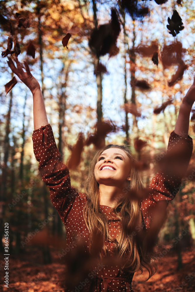 Happy beautiful woman throwing autumn leaves in the forest