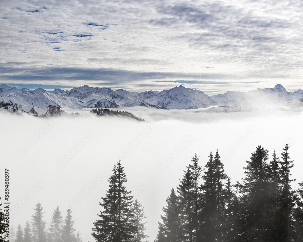 Snow covered mountains with inversion valley fog and trees shrouded in mist. Scenic snowy winter landscape in Alps, Allgau, Kleinwalsertal, Bavaria, Germany.