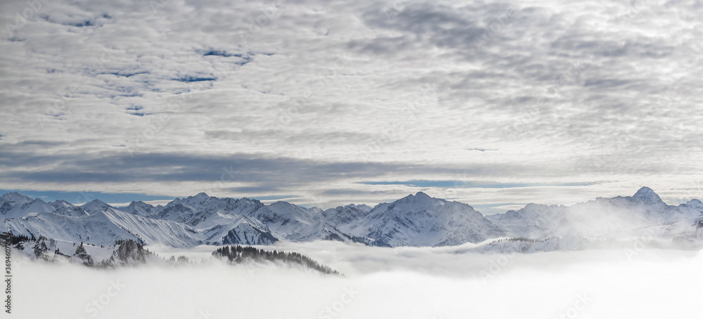 Snow covered mountains with inversion valley fog and trees shrouded in mist. Panoramic snowy winter landscape in Alps, Allgau, Kleinwalsertal, Bavaria, Germany.