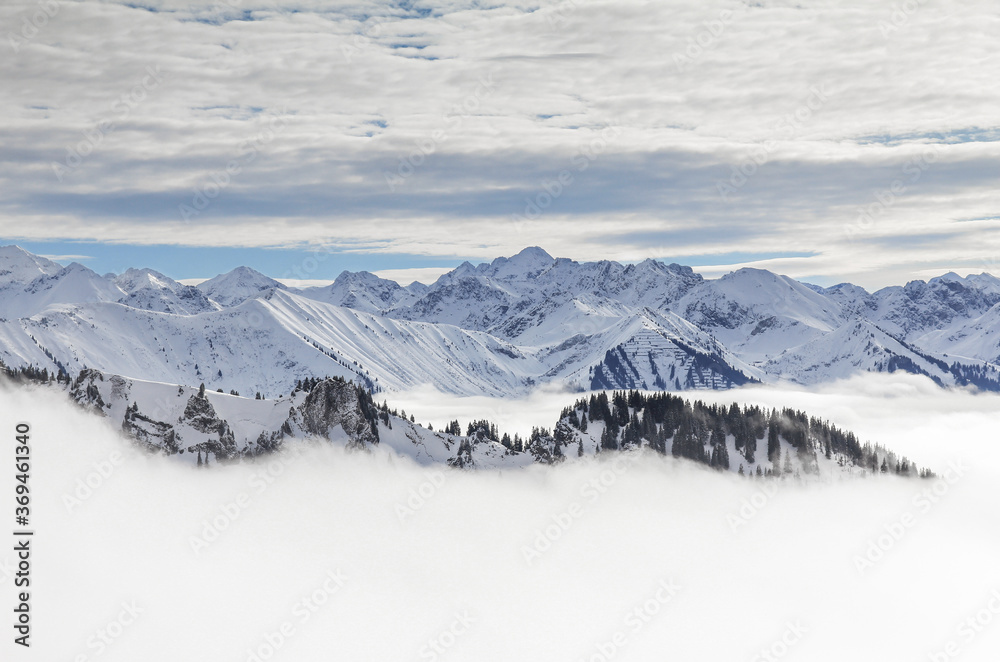 Snow covered mountains with inversion valley fog and trees shrouded in mist. Scenic snowy winter landscape in Alps, Allgau, Kleinwalsertal, Bavaria, Germany. Snow covered mountains with inversion valley fog and trees shrouded in mist. Scenic snowy winter landscape in Alps, Allgau, Kleinwalsertal, Bavaria, Germany.