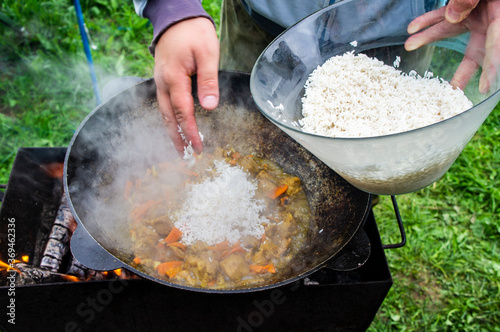 Cooking rice with meat and vegetables in a metal wok. The cook puts white rice with his hand.