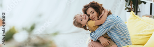 horizontal image of happy nanny hugging smiling kid while sitting on sofa