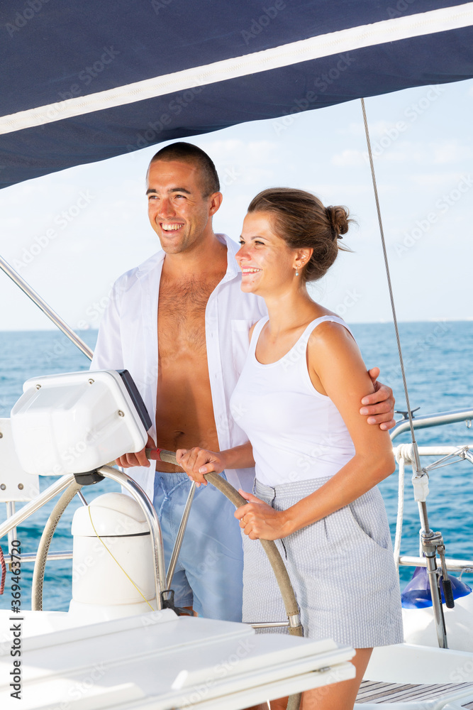 Loving couple steering yacht in calm blue ocean during romantic summer vacation