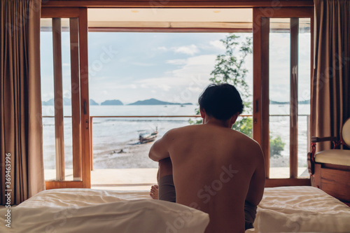 Asian man wake up in the room with sea view in the morning. Concept of vacation.