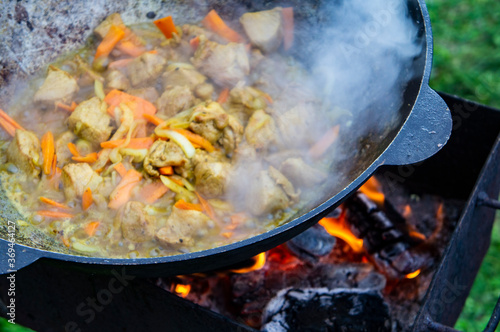 Cooking food on an open fire in a cauldron. Meat with vegetables is fried in a metal wok