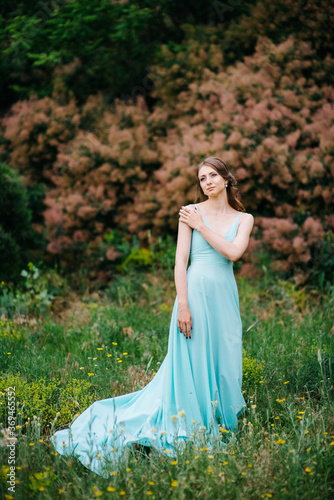 Happy girl in a turquoise long dress in a green park