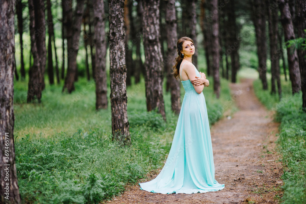 Happy girl in a turquoise long dress in a green park