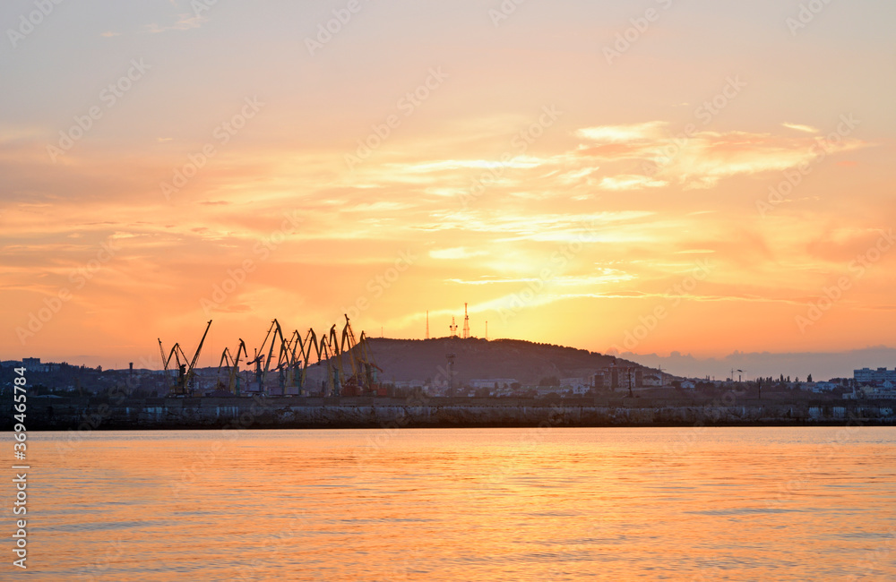 View of silhouettes of cranes and a hill against the sky