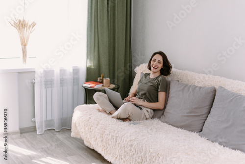 Enjoying time at home. Beautiful young smiling woman working on laptop sitting in a comfortable sofa at home