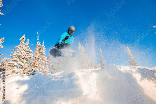 Man Snowboarder is jumping on winter forest against blue sky