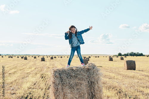 A cute little girl listens to music and dances on a haystack.