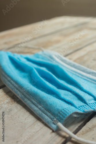 A close-up of a blue medical mask isolated on a wooden table. Face mask protection against pollution, virus, flu, and coronavirus. Health care and surgical concept.