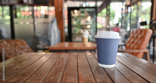 Take Away coffee cup on wooden table with blurred cafe background.