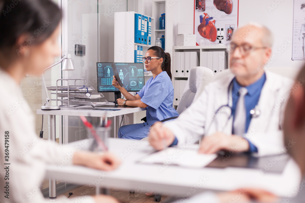 Obraz premium Nurse examining patient x-ray. Senior doctor in hospital office explaining diagnosis to disabled man in wheelchair and his wife. Mature medic wearing white coat and stethoscope.