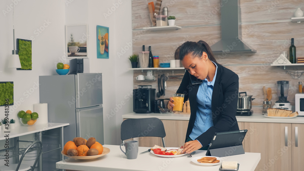 Businesswoman on phone while eating breakfast. Concentrated business woman in the morning multitasking in the kitchen before going to the office, stressful way of life, career and goals to meet