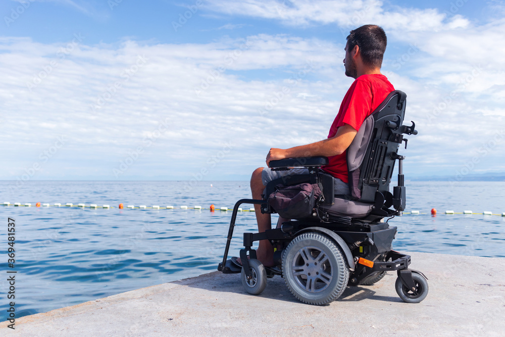 Man sitting in a wheelchair on the beach. Dangers of jumping into water from heights. Head and spine injury. Man sitting in a wheelchair on the beach. Dangers of jumping into water from heights. Head and spine injury.