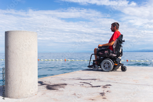 Man sitting in a wheelchair on the beach. Dangers of jumping into water from heights. Head and spine injury.