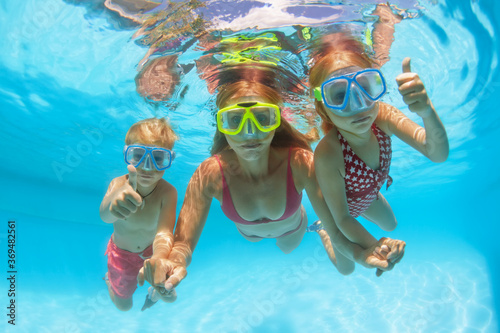 Happy people dive underwater with fun. Funny photo of mother, kids in snorkeling masks in aqua park swimming pool. Family lifestyle, children water sport activity, lesson with parent on summer holiday