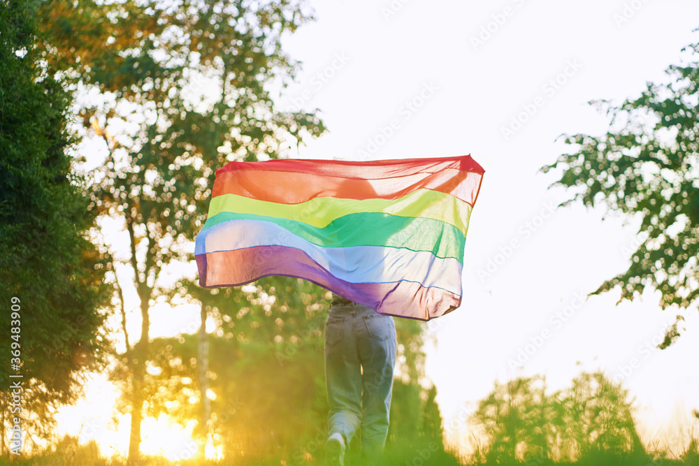 Woman running with rainbow lgbt flag behind back.