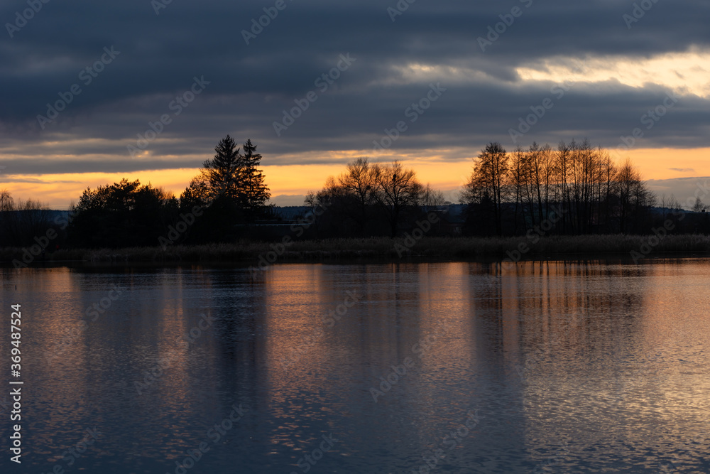 Dark clouds during sunset, reflection of trees in water