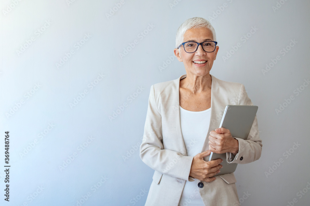 Head and shoulders view of beautiful older woman with short grey hair and beige jacket against grey background. Business woman with glasses smiling. Portrait of beautiful mature woman Head and shoulders view of beautiful older woman with short grey hair and beige jacket against grey background. Business woman with glasses smiling. Portrait of beautiful mature woman