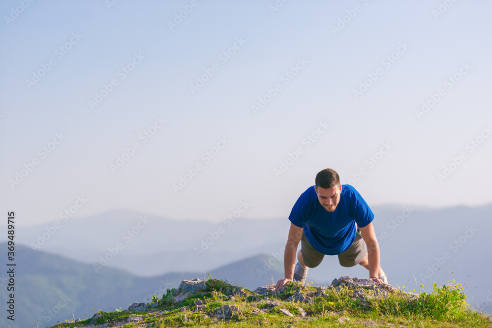 Fit male athlete doing pushups at the edge of a cliff while enjoying the amazing view.
