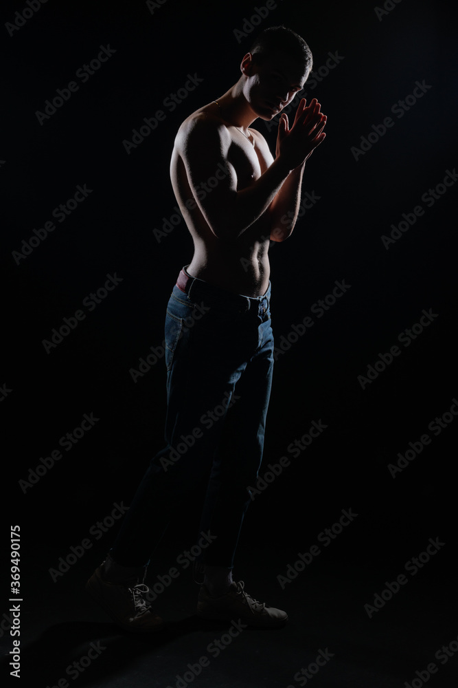 Silhouette picture of a hot shirtless muscular man posing in jeans in a dark studio.