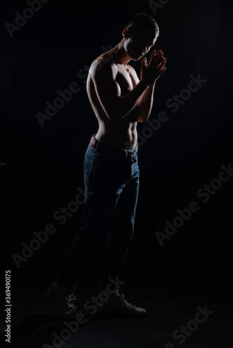 Silhouette picture of a hot shirtless muscular man posing in jeans in a dark studio. © qunica.com