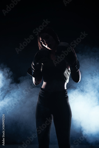 Fototapeta Naklejka Na Ścianę i Meble -  Silhouette portrait with white smoke in the background of a female model with boxing gloves