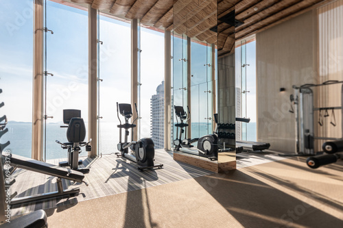 Exercise Bike and Treadmill Equipment in Modern Gym with views of Sea and Sky in Background of Large Glass Windows, The sun's rays penetrated the big window into the luxury gym. photo